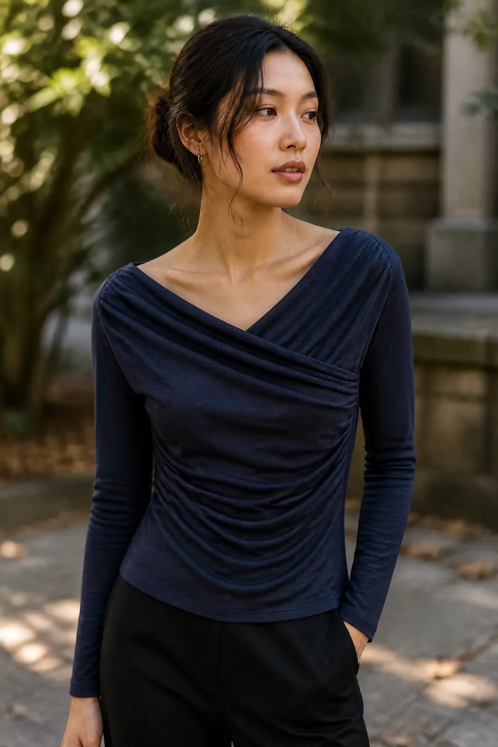 Fashionable woman in deep navy draped surplice top in outdoor setting with soft lighting