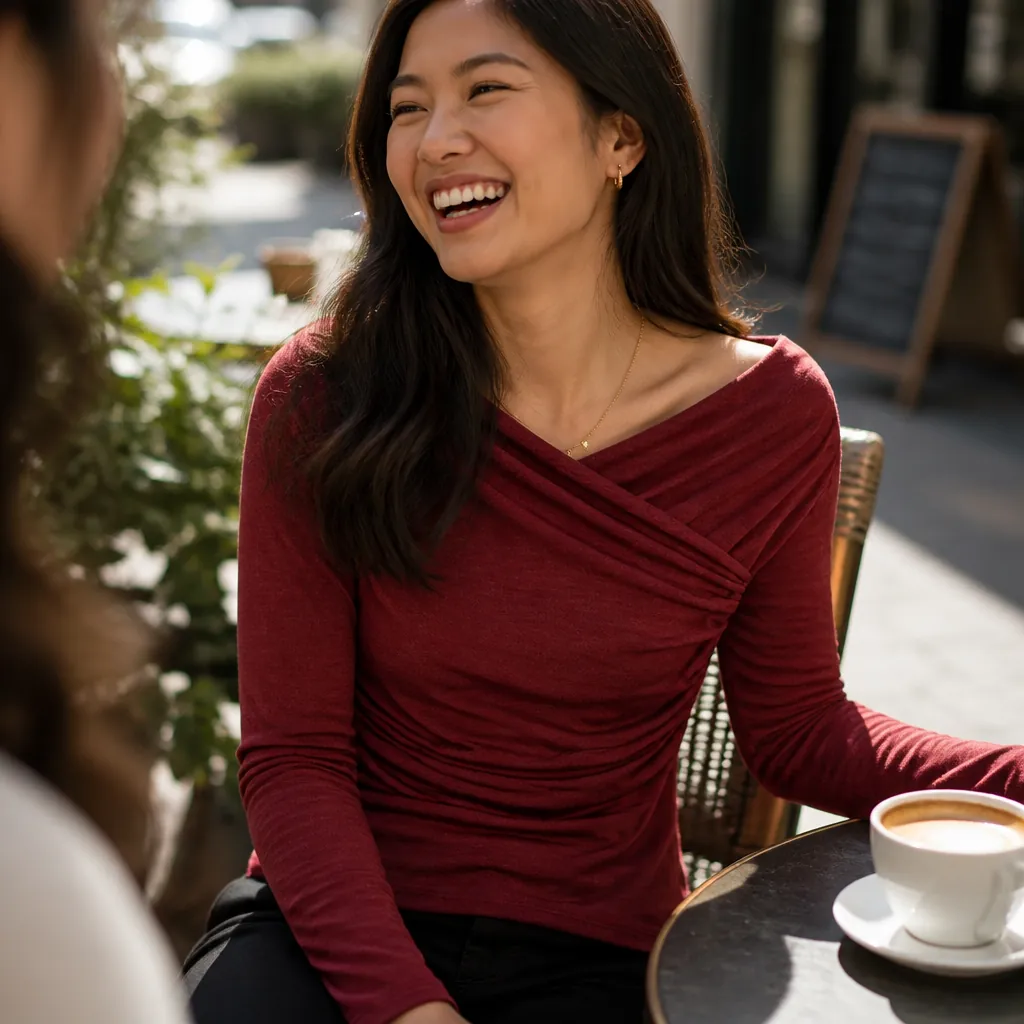 Joyful woman in elegant black draped top at cafe with friends laughing