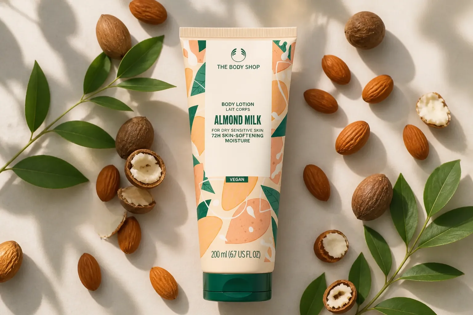 Flat lay of almond milk body lotion tube surrounded by almonds and shea nuts with botanical elements