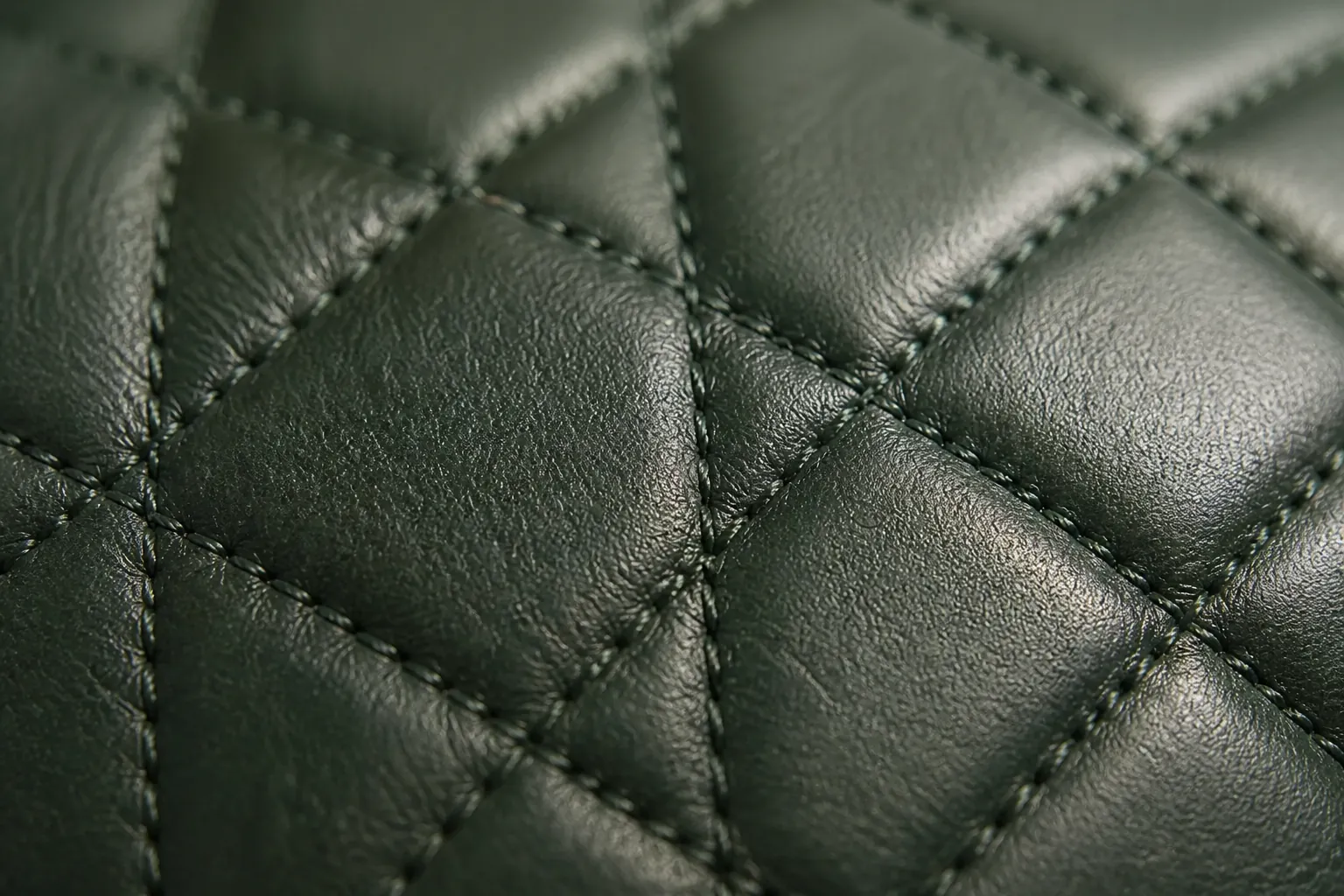 Close-up macro photograph of quilted leather texture showing diamond stitch pattern with soft ambient lighting
